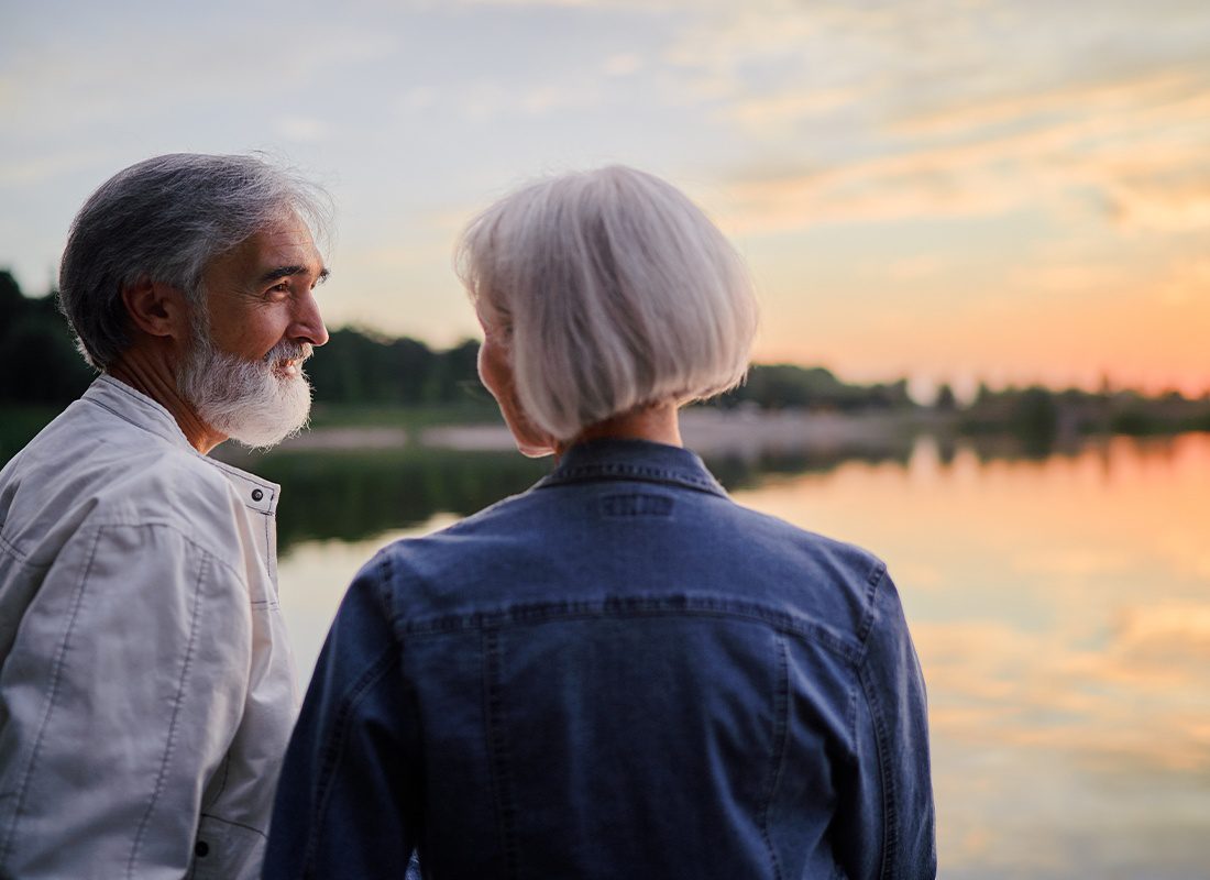 Clayton, NY - Senior Couple Sitting Together on a Lake Bank Enjoying the Sunset